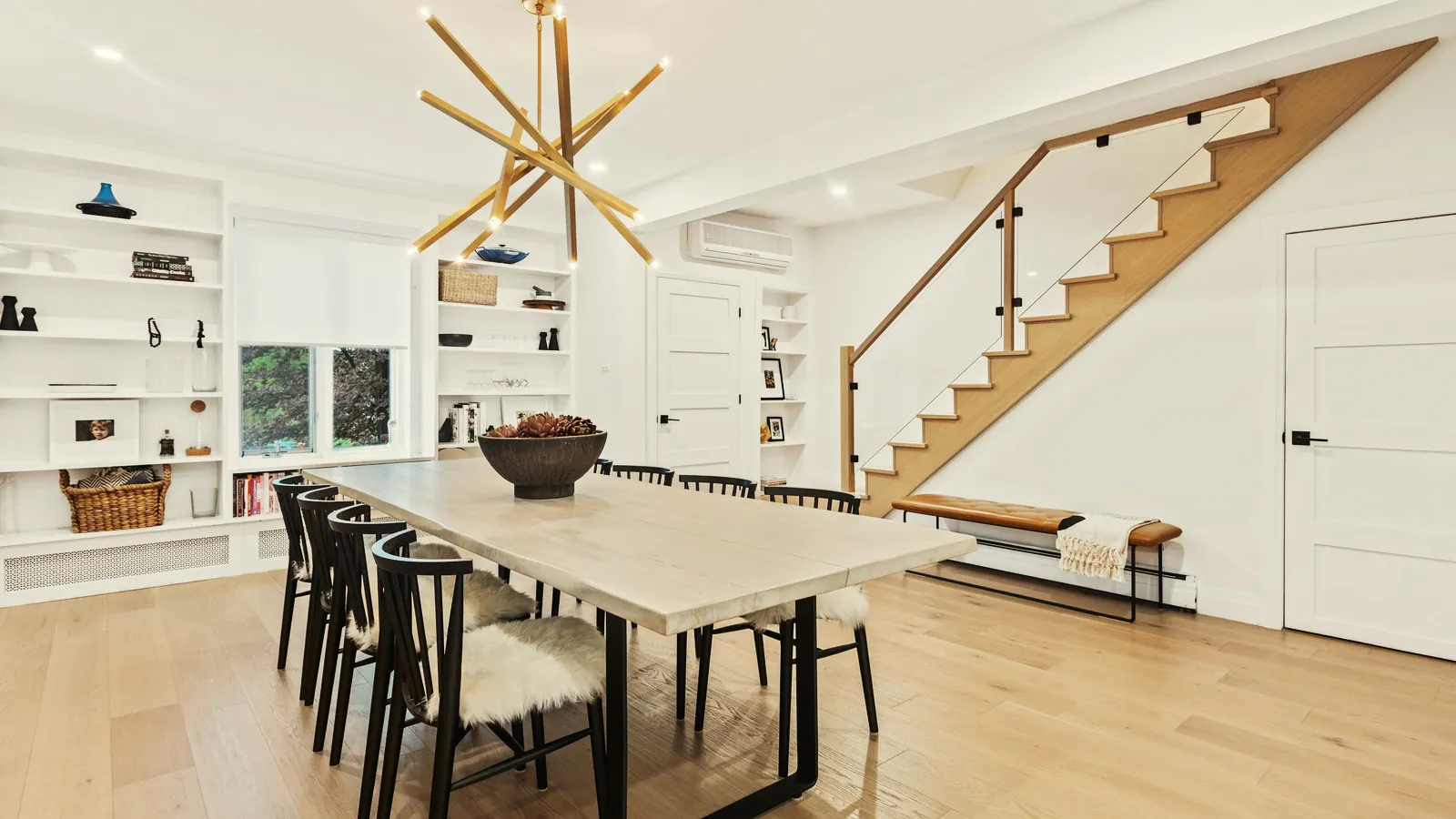 Lichte eetkamer met een lange tafel en een open houten trap langs de wand